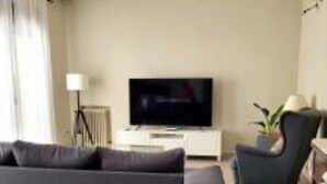 Una sala moderna con un sofá oscuro, un televisor, una lámpara y un sillón.