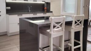 Una cocina moderna con armarios blancos, encimera negra y dos taburetes blancos.