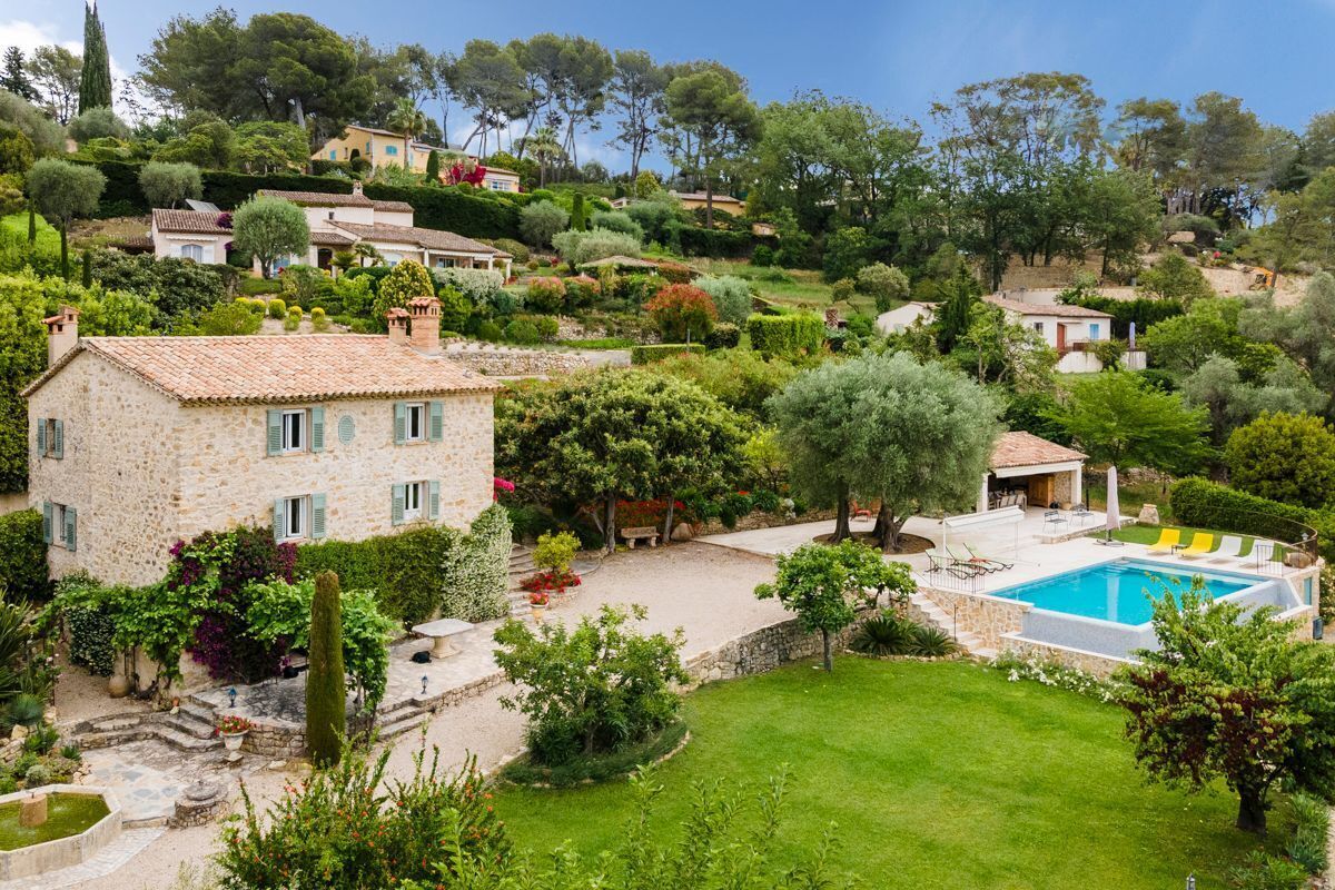Une maison en pierre avec une piscine, entourée d’une végétation luxuriante et d’autres maisons sur une colline.