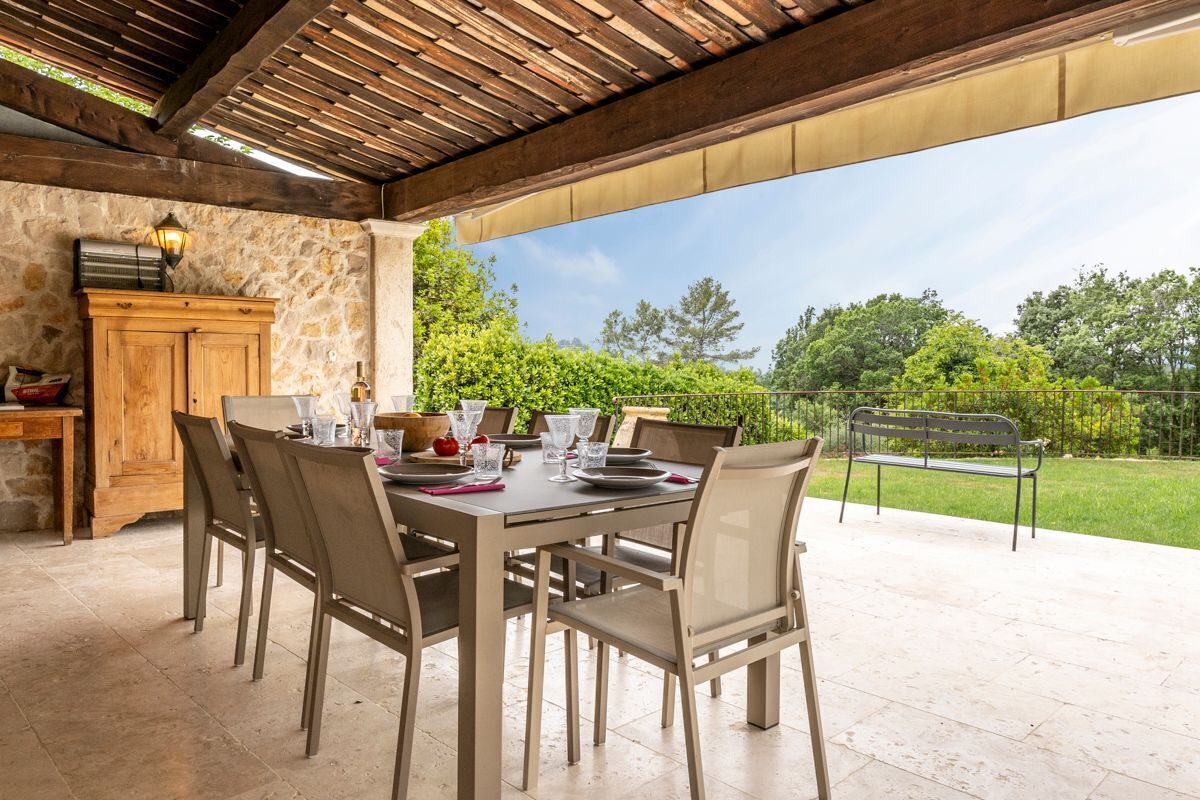 Une terrasse extérieure avec un mur en pierre, une table en bois et des chaises, donnant sur un jardin.