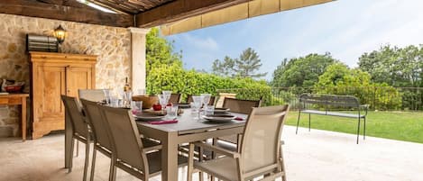 Une terrasse extérieure avec un mur en pierre, une table en bois et des chaises, donnant sur un jardin.