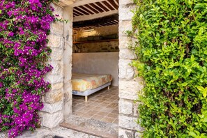 Une pièce aux murs de pierre, avec un lit, un plafond en poutres apparentes et une petite fenêtre.