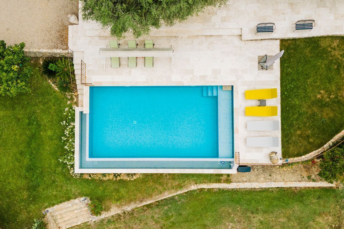 An aerial view of a swimming pool area with a rectangular pool, a seating area with chairs, and a small deck with a table and chairs.