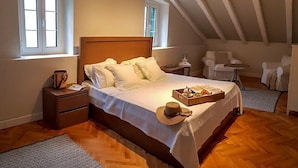A bedroom with a wooden bed, two bedside tables, a window, and a small seating area with a table and chairs.