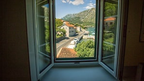 A room with a large window offering a view of a coastal town, a road, and a body of water.