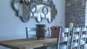 A dining area with a wooden table, white chairs, a decorative mirror, a vase with flowers, and a candle on the table.