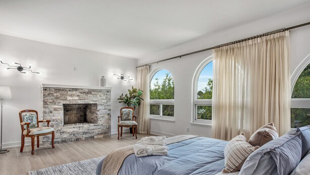 Un dormitorio con chimenea de piedra, una cama grande, vista a árboles y una lámpara moderna.