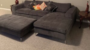 Un sofá seccional gris con otomanas a juego, una mesita de madera y un jarrón con flores rojas.