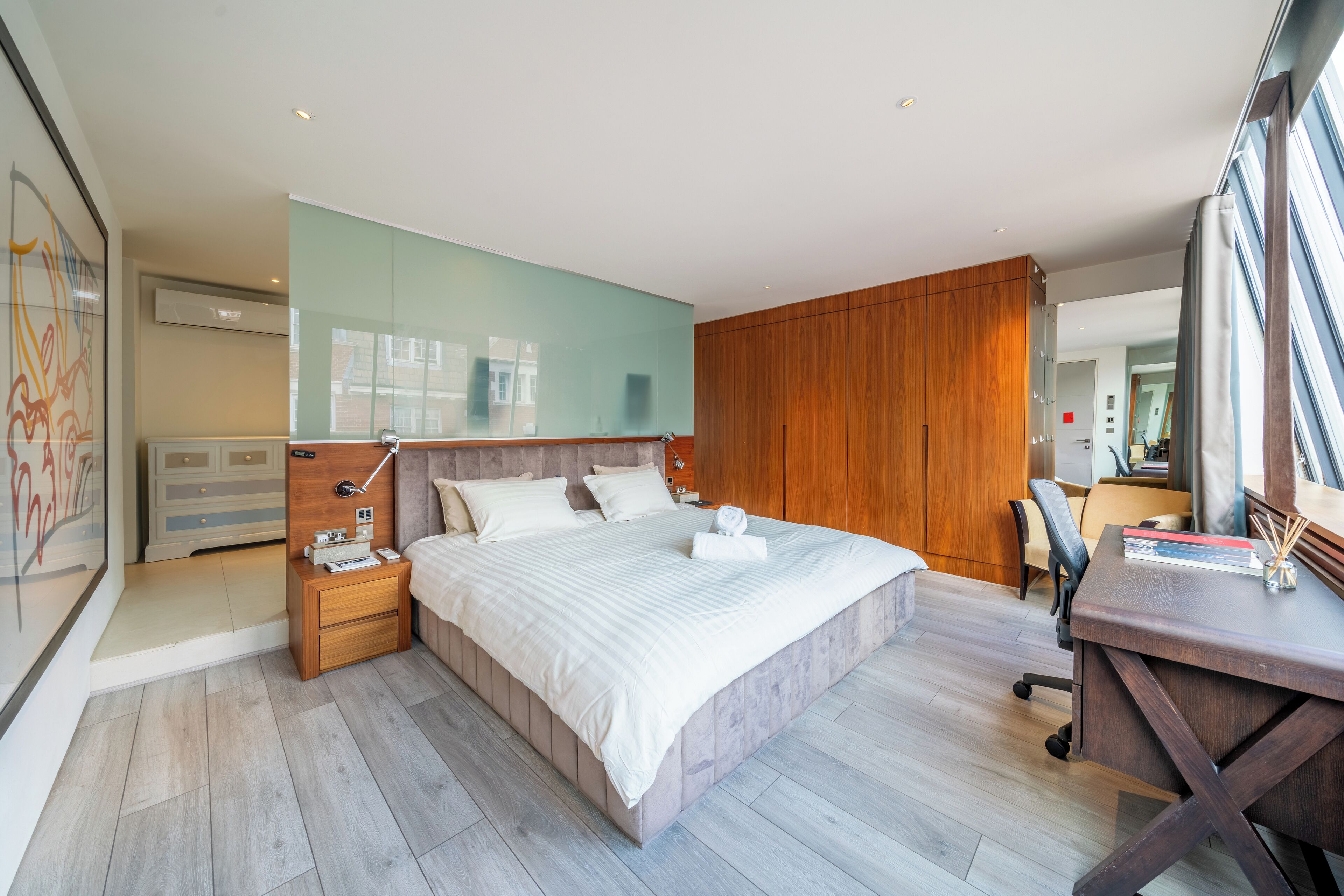 Una camera da letto moderna con un letto grande, una testiera in legno, comodini e una scrivania con una sedia.