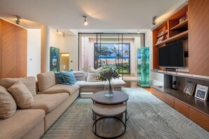 A modern living room with a beige sofa, a round coffee table, and a flat-screen TV on a wooden cabinet. - The One Chelsea (London)