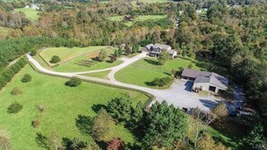 An aerial view of a property with a winding driveway, a large grassy area, and a house with a garage.