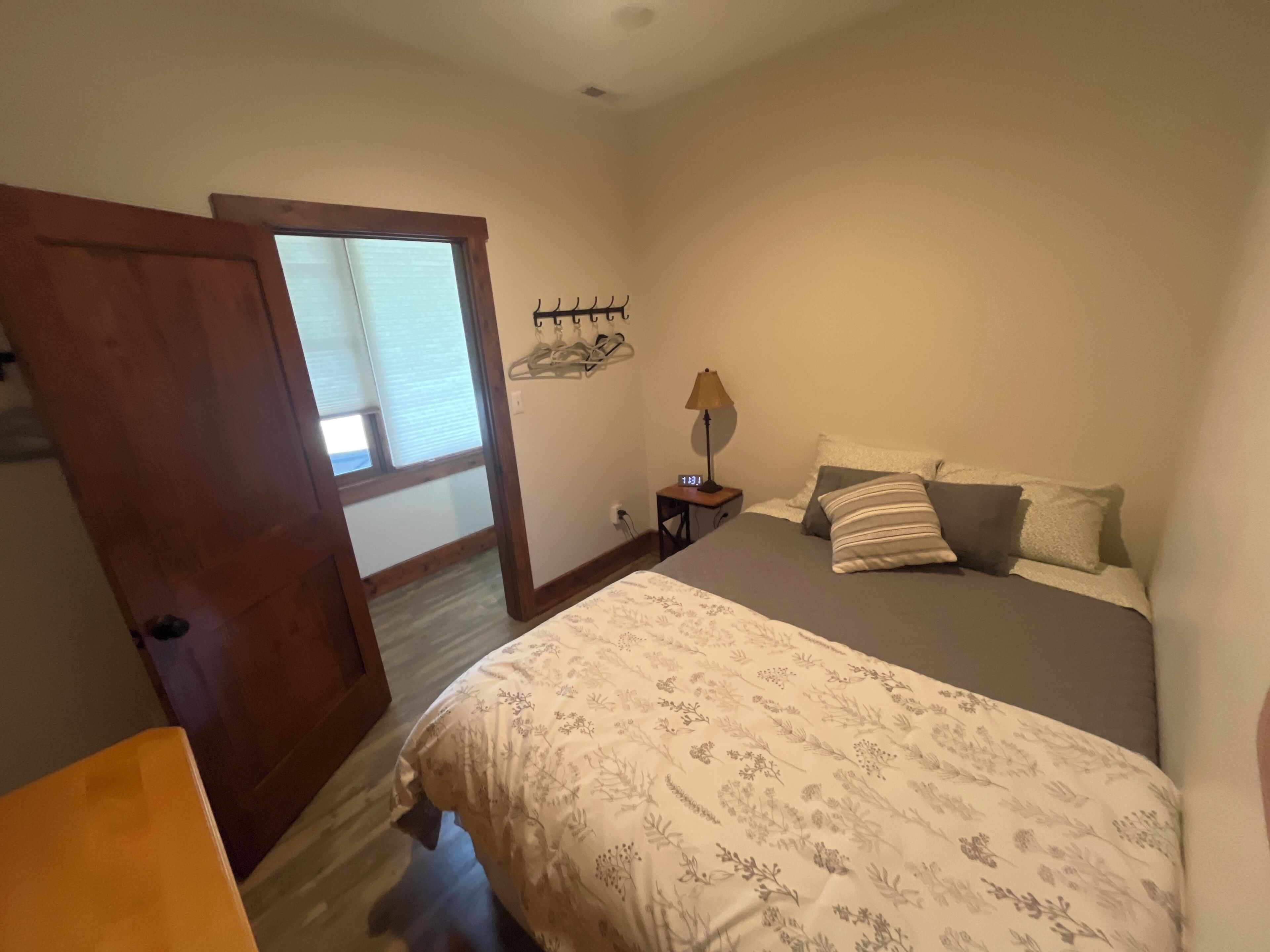 Een slaapkamer met een bed, nachtkastje, lamp, klok en een deur die naar een andere kamer leidt.