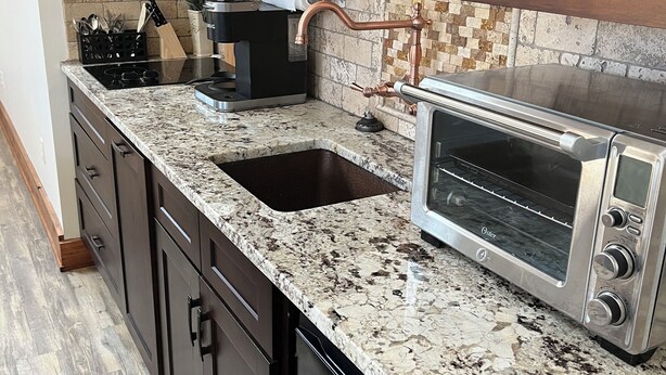 A kitchen with granite countertops, a stainless steel toaster oven, a sink, and dark cabinetry.