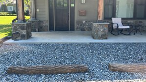 A covered patio with a stone column, a wooden swing chair, and a stone table.
