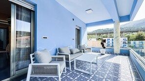 A balcony with a blue and white tiled floor, a sofa, a small table, and a potted plant.