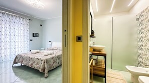 A hotel room with a bed, a bedside table with a sink, a toilet, and a shower area.
