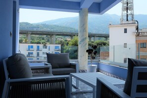 A balcony with seating, a potted plant, and a view of a bridge and mountains.