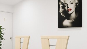 Quarto com porta branca identificada com o número 5, uma mesa preta e duas cadeiras de madeira. Um retrato em preto e branco está na parede.
