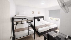 Quarto com beliches, escrivaninha, cadeira, ventilador e janela com vista.