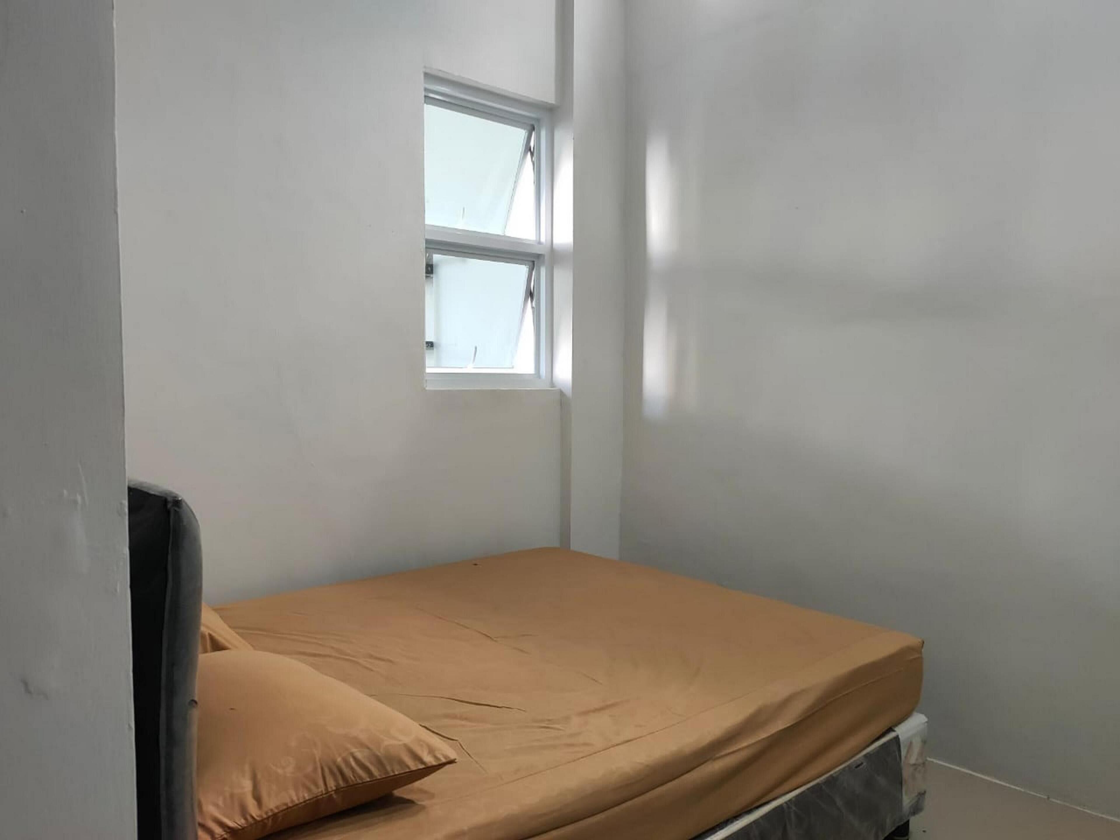 A small, single-bed room with a window and a bed covered in a beige sheet.