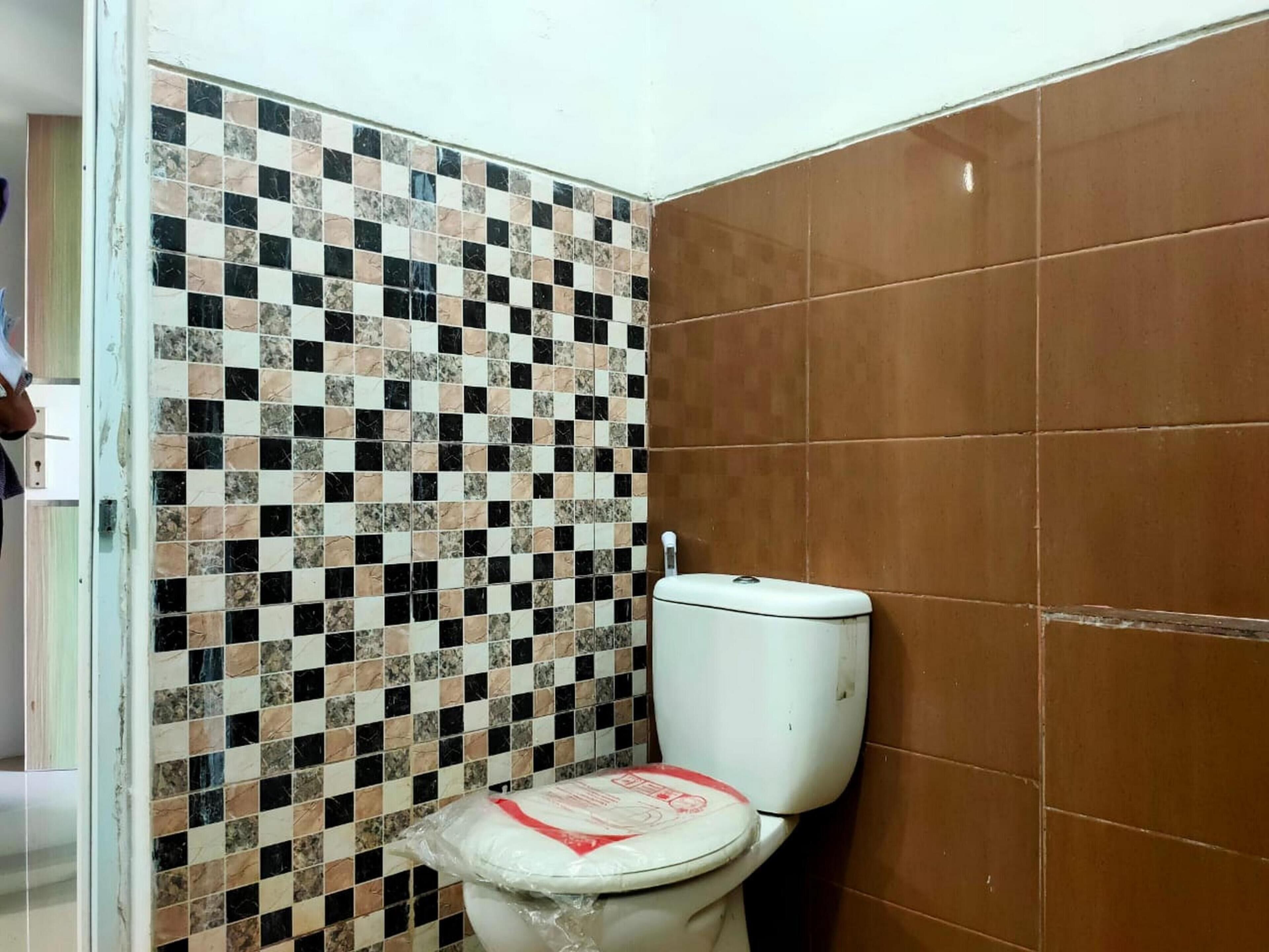 Et badeværelse med mosaikbeklædt væg, toilet og brune fliser.