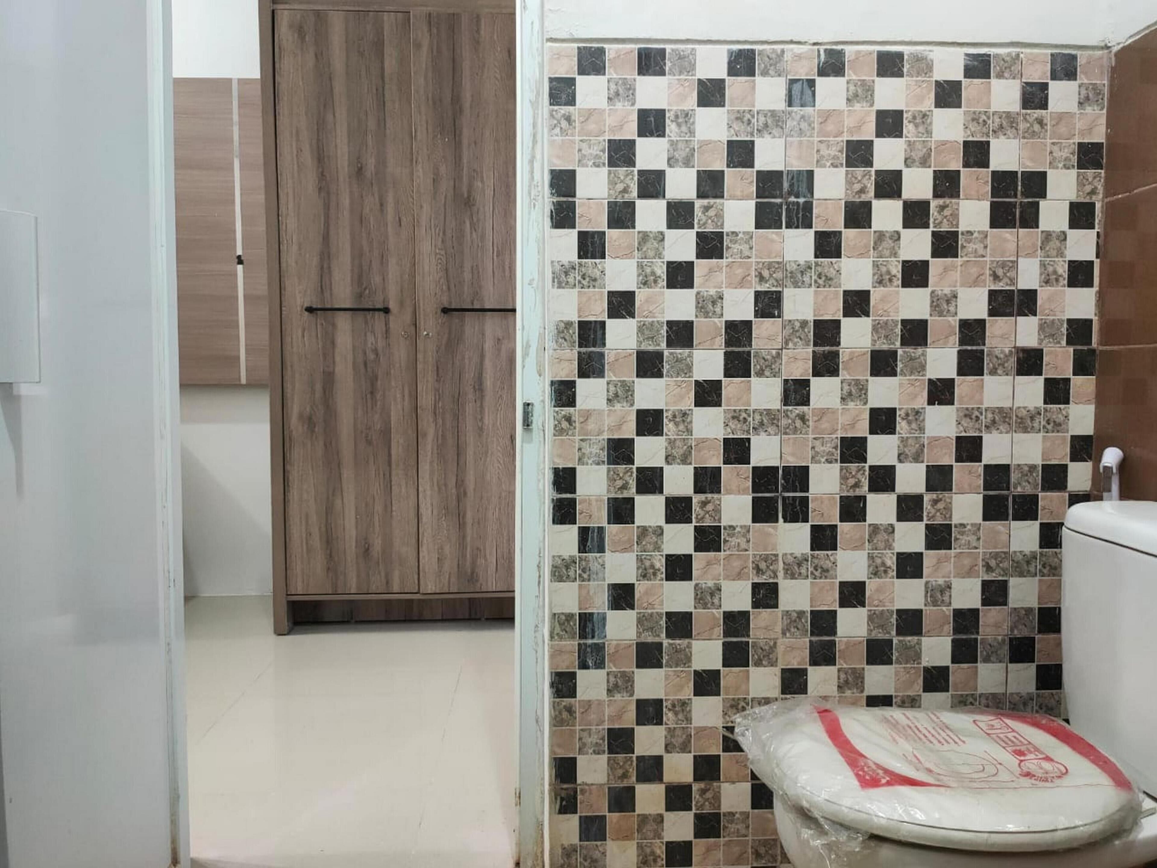 Een badkamer met een betegelde douchewand, een toilet en een houten garderobe.