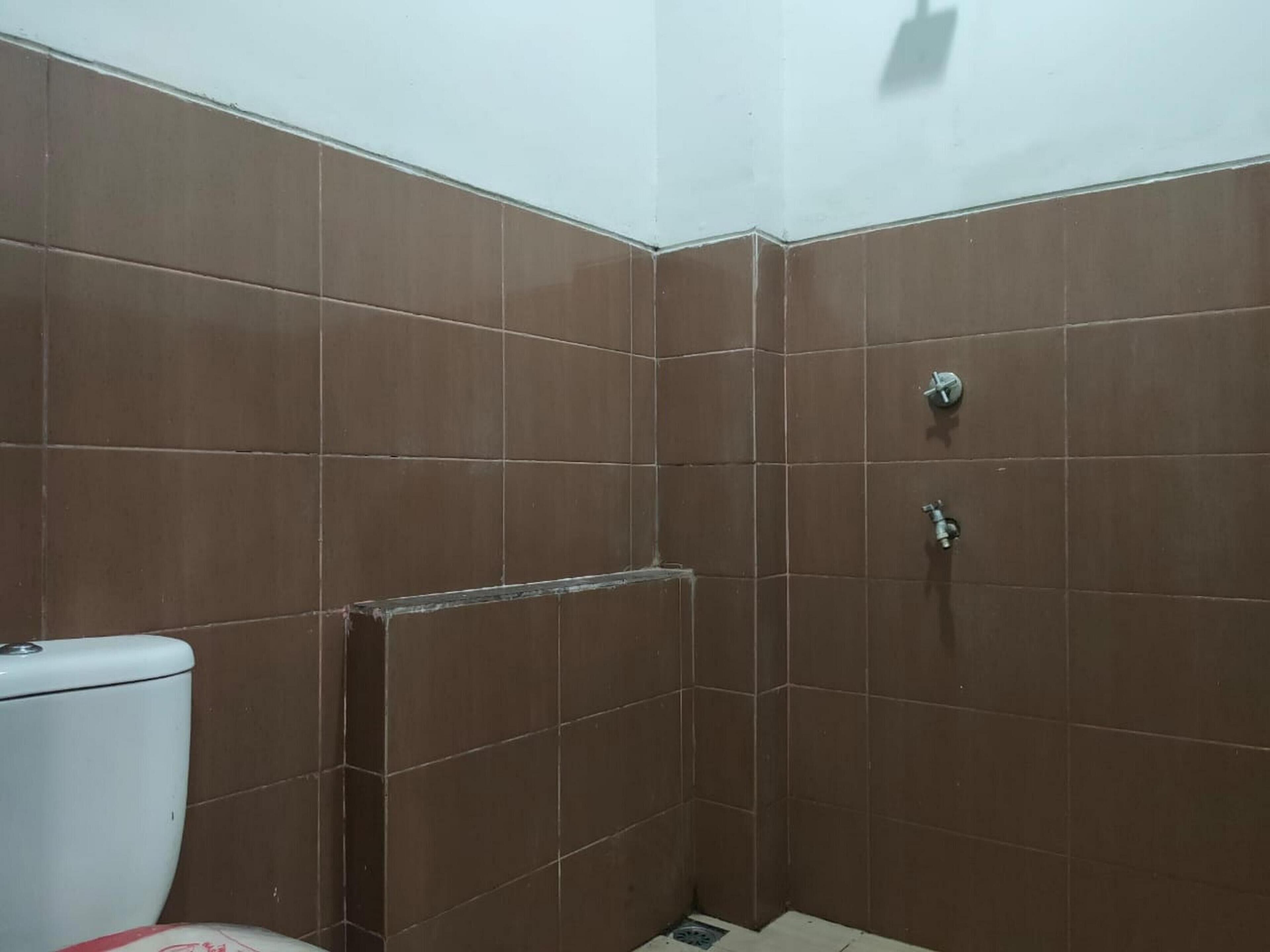 Et lille badeværelse med eget toilet, beklædt med brune fliser, samt et bruseområde med afløb.