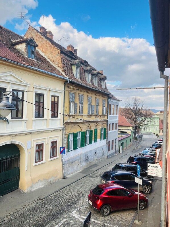 A street view with historic buildings, cobblestone pavement, and parked cars.
