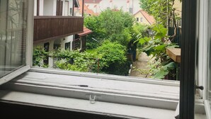 Une vue depuis une fenêtre donnant sur une cour intérieure bordée de bâtiments, avec notamment un balcon doté d’une balustrade en bois.