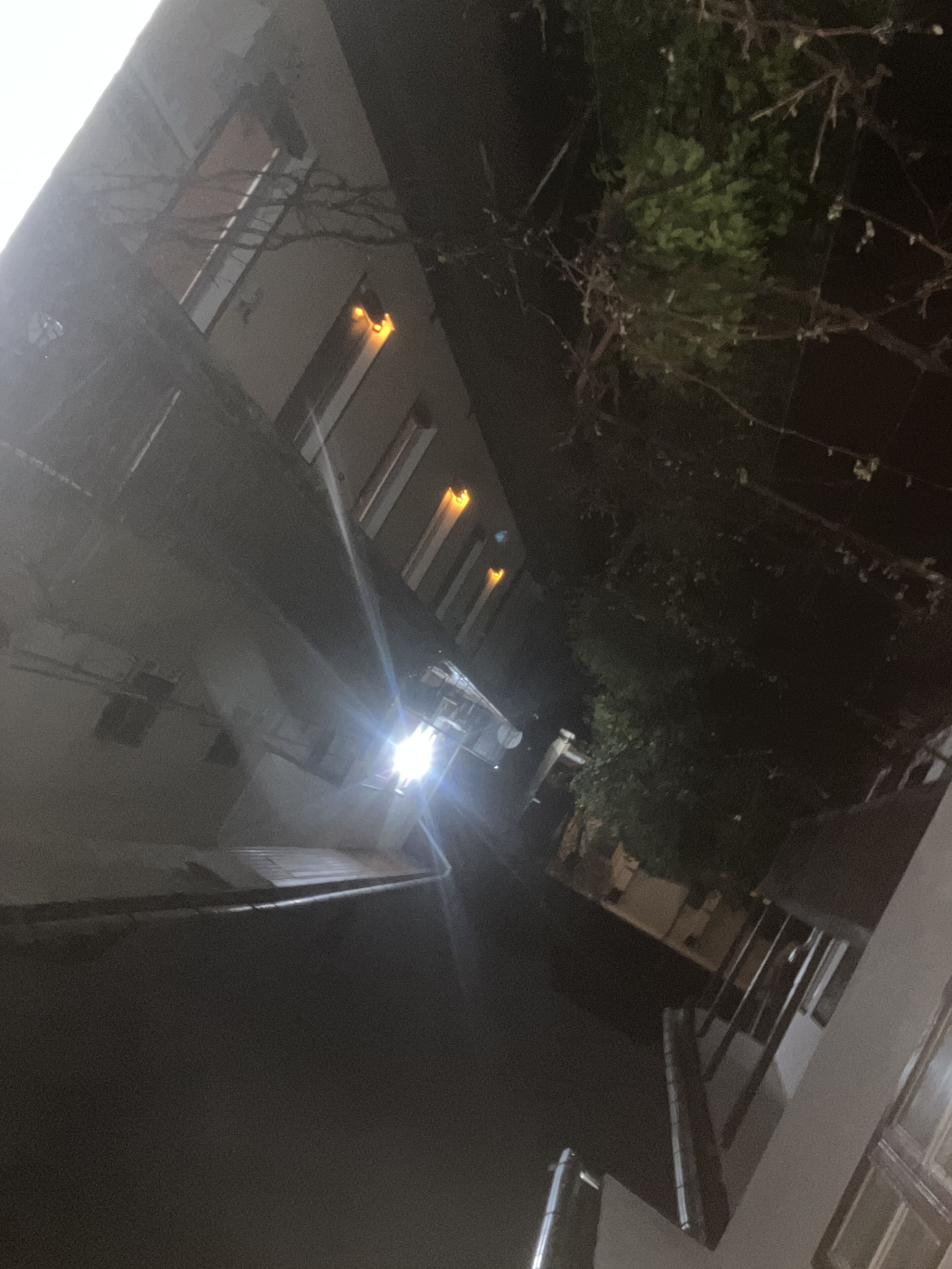 A nighttime street view with buildings, a car, and a bright light source.