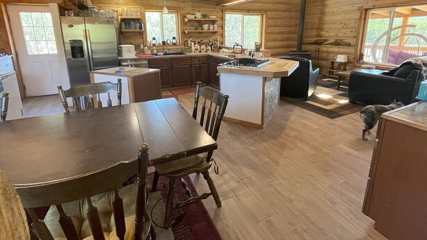 Interno di una baita con arredamento in legno, zona pranzo, cucina e soggiorno con un divano e un cane.