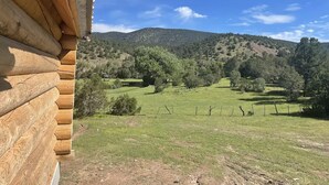 Una baita di legno con vista su un prato verde e colline sullo sfondo.