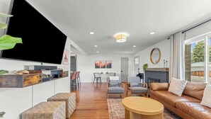 Un salon moderne avec un canapé, une table basse et un téléviseur. On aperçoit au fond une cheminée, un coin repas et une cuisine.