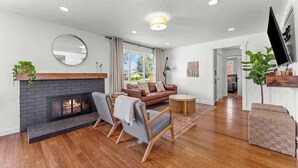Un salon moderne avec une cheminée, un canapé, deux fauteuils, une table basse et un téléviseur fixé au mur.