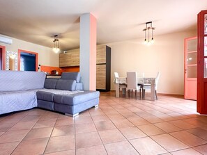 A living room with a grey sectional sofa, a dining table with chairs, and a kitchen area in the background. - the Phoenix apartment (Vaccarolo)