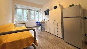 Eine kleine, kompakte Küche mit Kühlschrank, einem Esstisch mit Stühlen und einem Fenster mit Vorhängen.