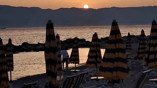Ein Strandbild mit gestreiften Sonnenschirmen und einem Sonnenuntergang über dem Wasser.