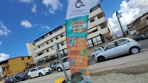 Ein barrierefreies Schild mit Informationen auf Italienisch, platziert auf einer Betonfläche. In der Nähe stehen zwei schwarze Mülleimer.