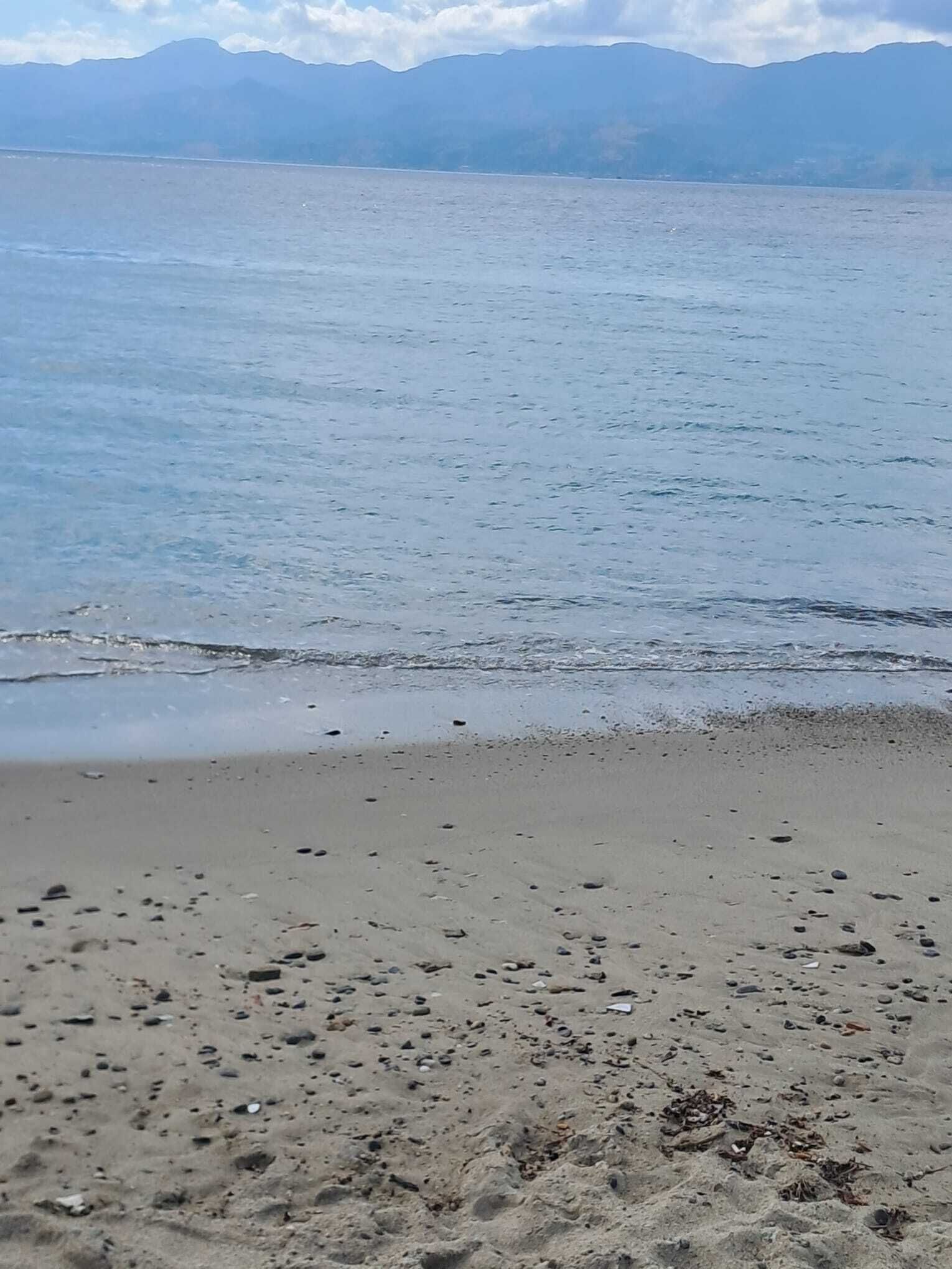 A beach with a calm sea and distant mountains.