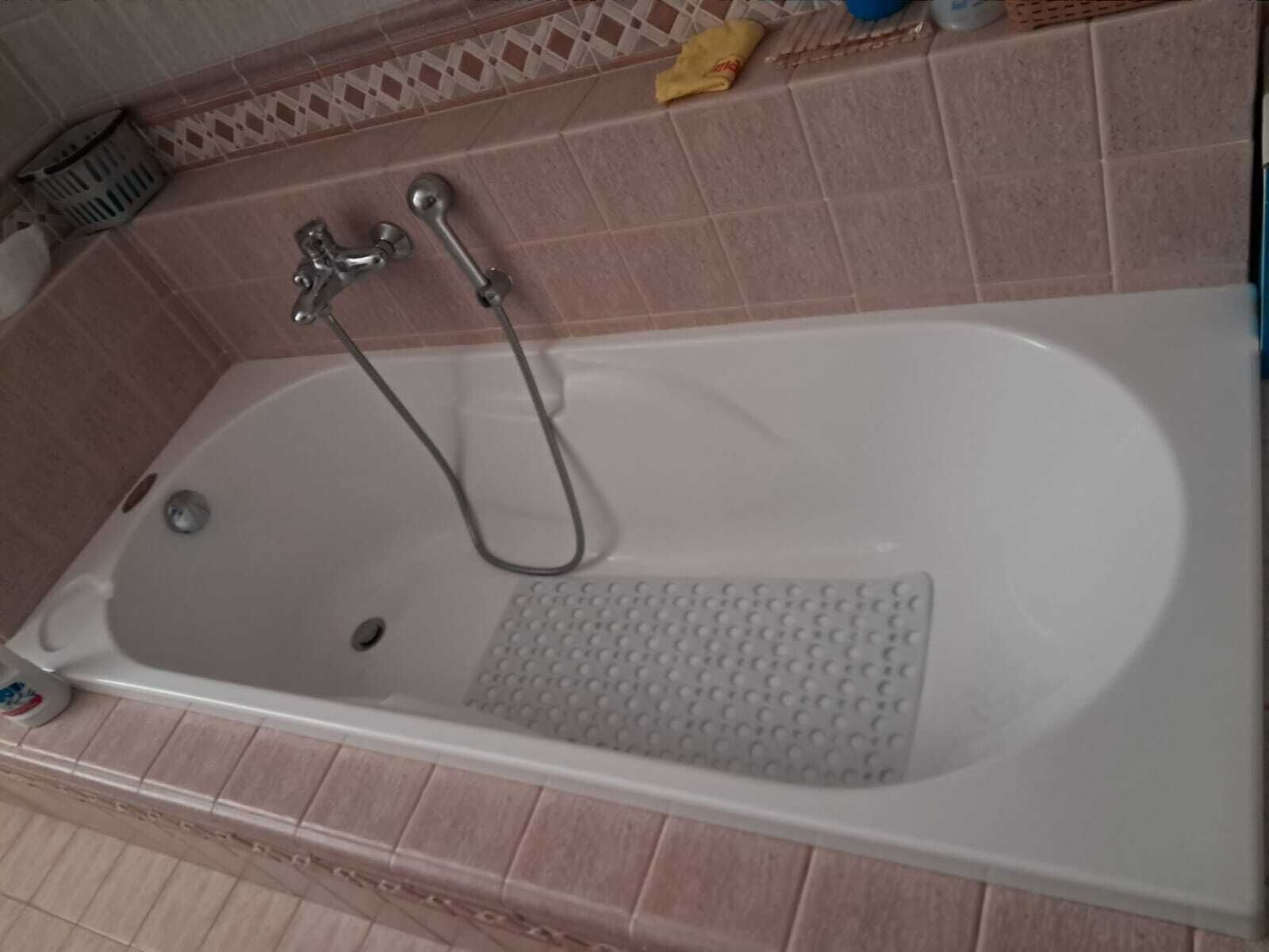 Ein Badezimmer mit einer weißen Badewanne, einer Duschbrause und einer integrierten Sitzgelegenheit.
