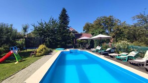 A rectangular swimming pool with a clear blue water surface, surrounded by a wooden deck. There are lounge chairs and umbrellas for sunbathing. - Holiday apartment with outdoor pool and air conditioning (Balatonföldvár)