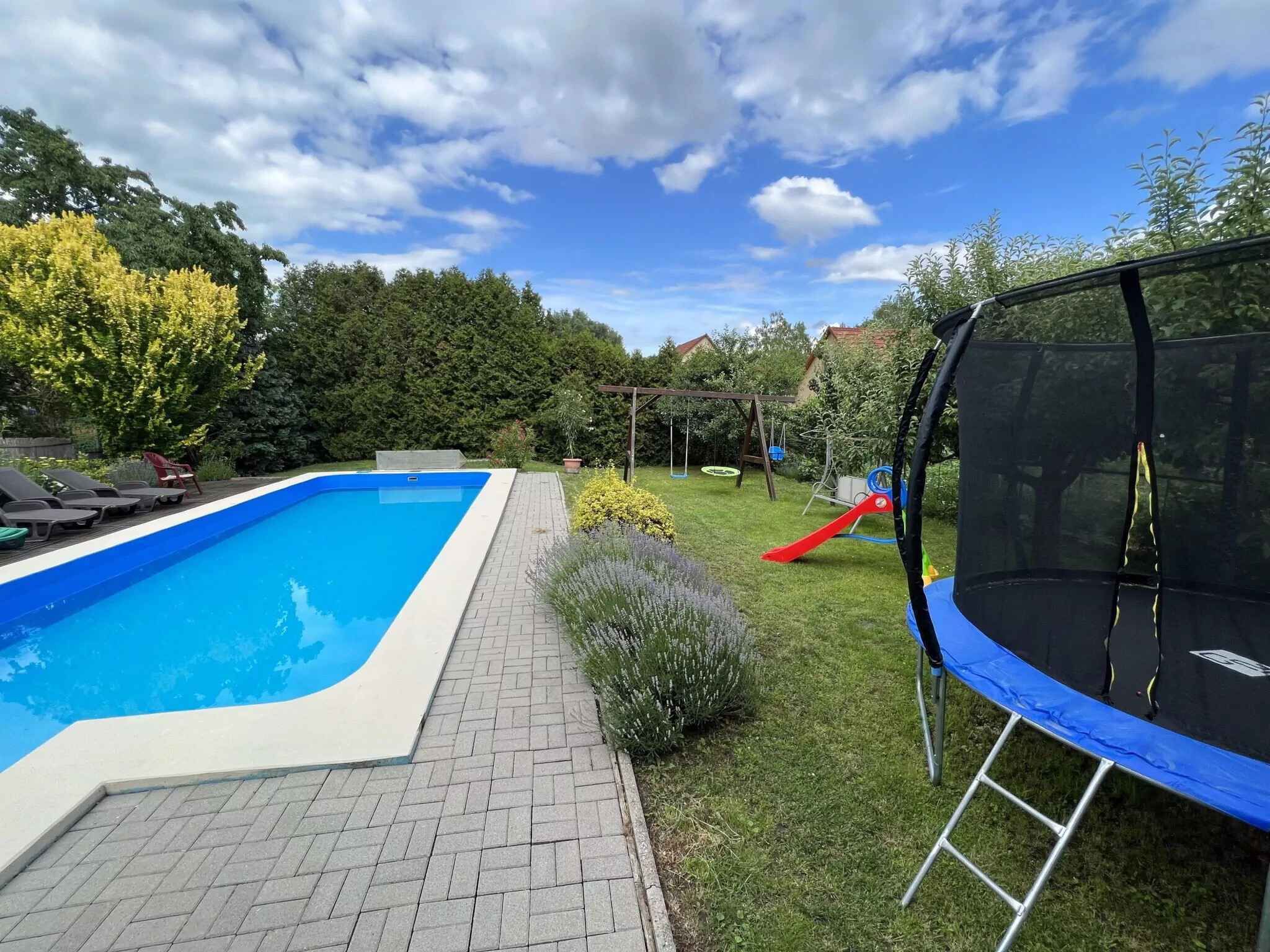 Een achtertuin met een zwembad, een trampoline en een glijbaan.