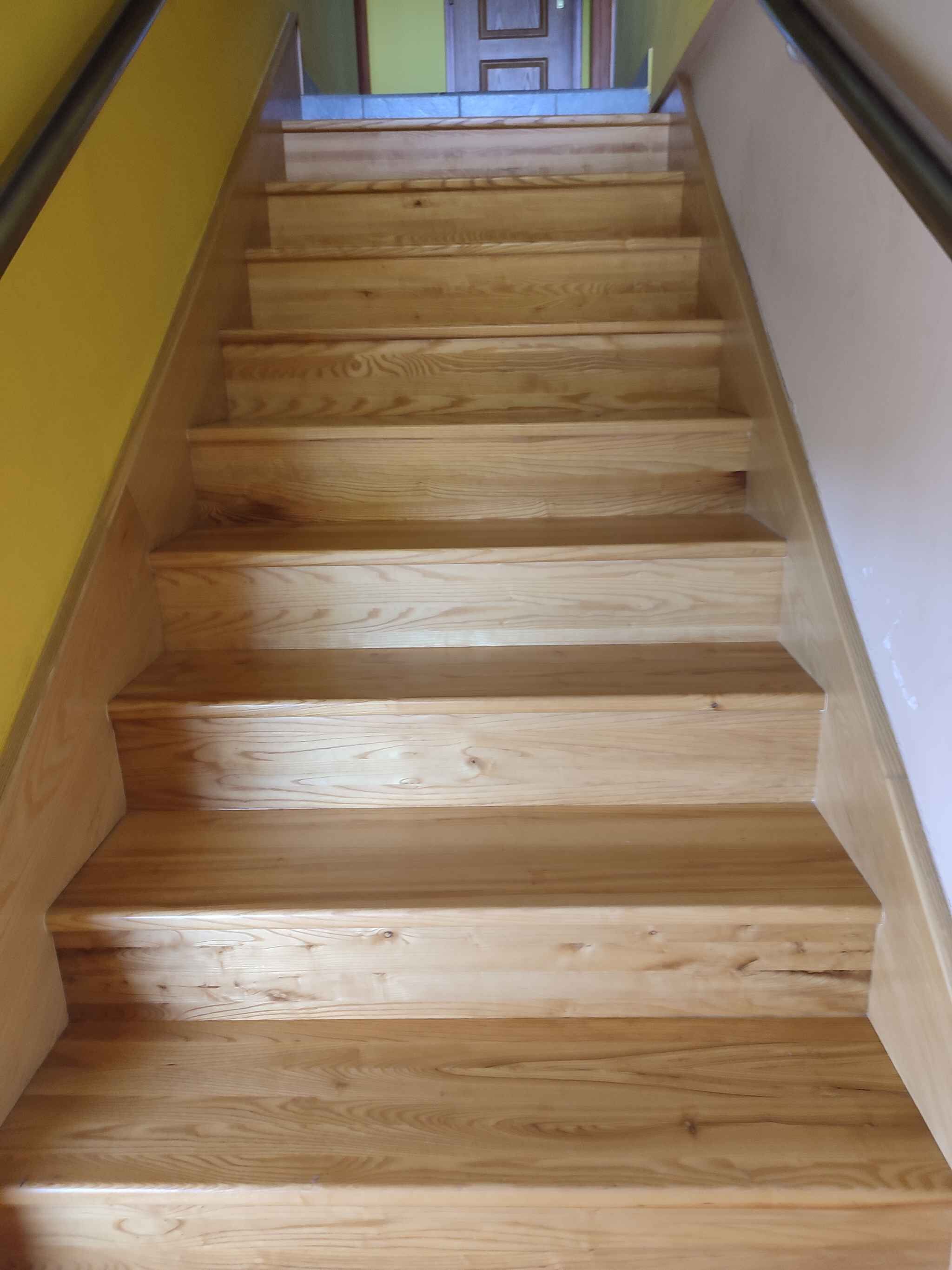 Eine Holztreppe mit Geländer auf der rechten Seite, die zu einer Tür oben führt.