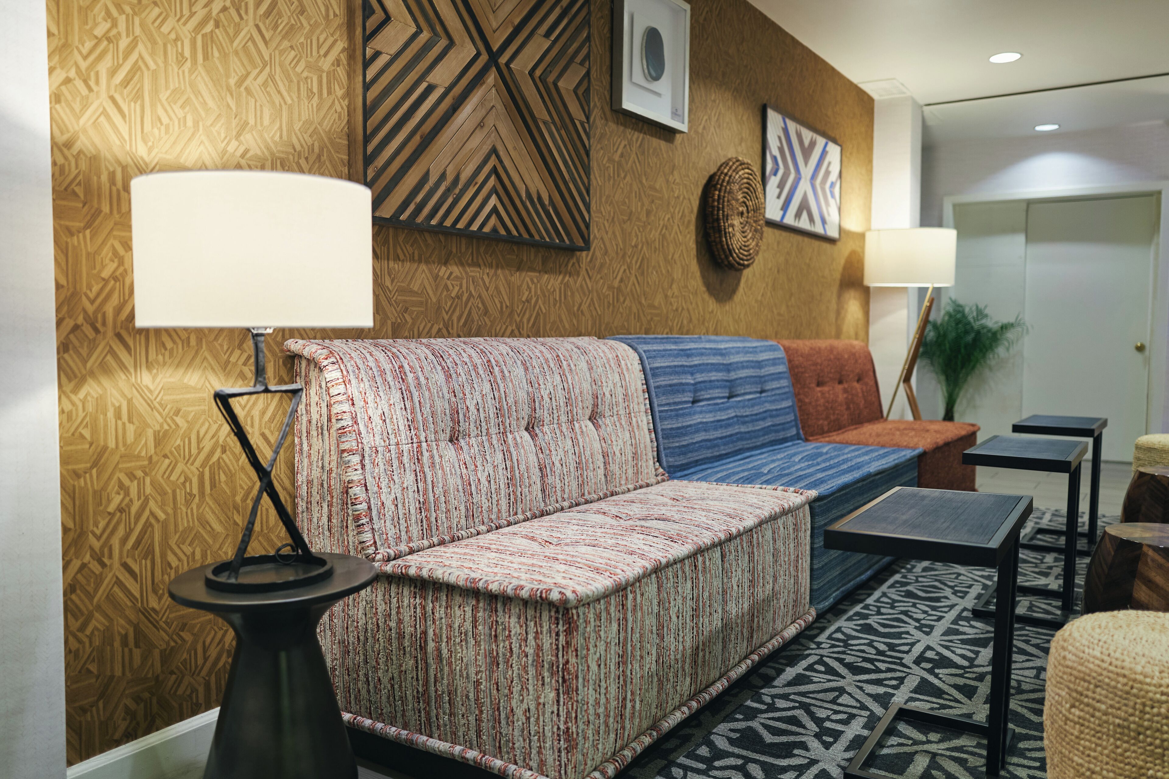Een moderne lobby met een patroonwand, een bank met gestreept kussen, een ronde tafel en een kleine potplant.