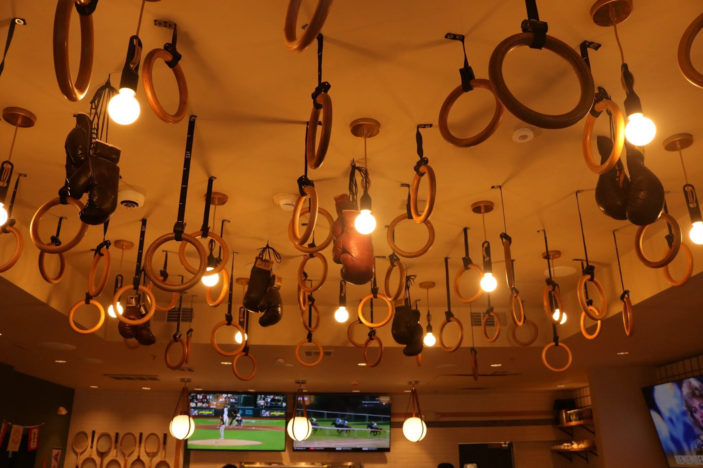 A ceiling with multiple rings and lights, a television screen displaying a sports event, and a wall with various items.