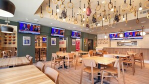 A restaurant with multiple tables and chairs, hanging rings, and televisions displaying news. - Soma House (San Francisco)