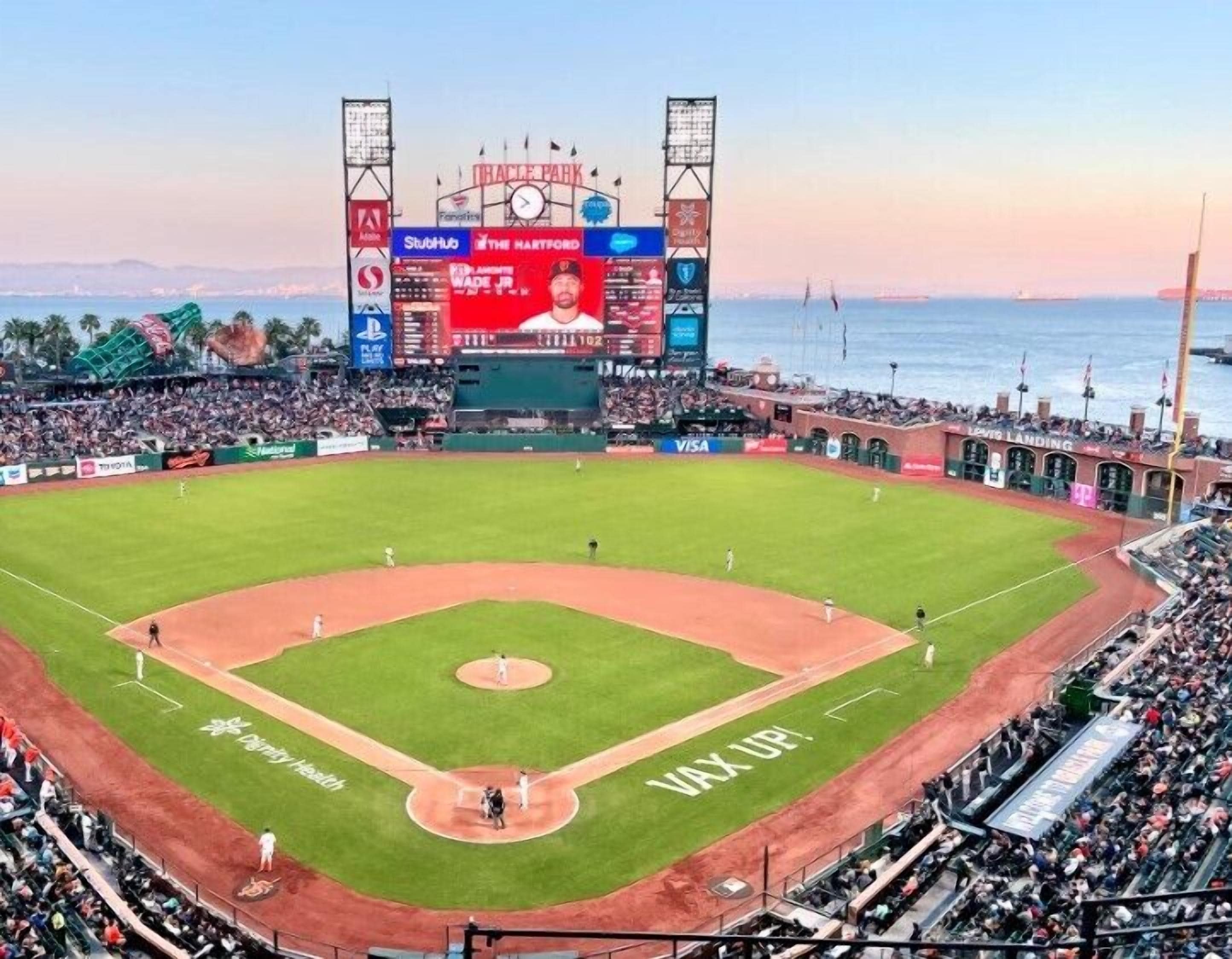 Un estadio de béisbol con un marcador grande, publicidad y una multitud de espectadores.