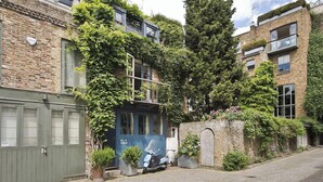 A brick building with ivy-covered walls, a blue door, and a scooter parked outside.