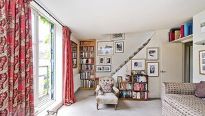 A cozy living room with a large window, a staircase, and a bookshelf filled with books.