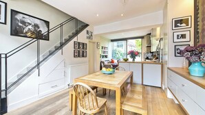 A modern kitchen with a wooden table, chairs, and a staircase with black railings.